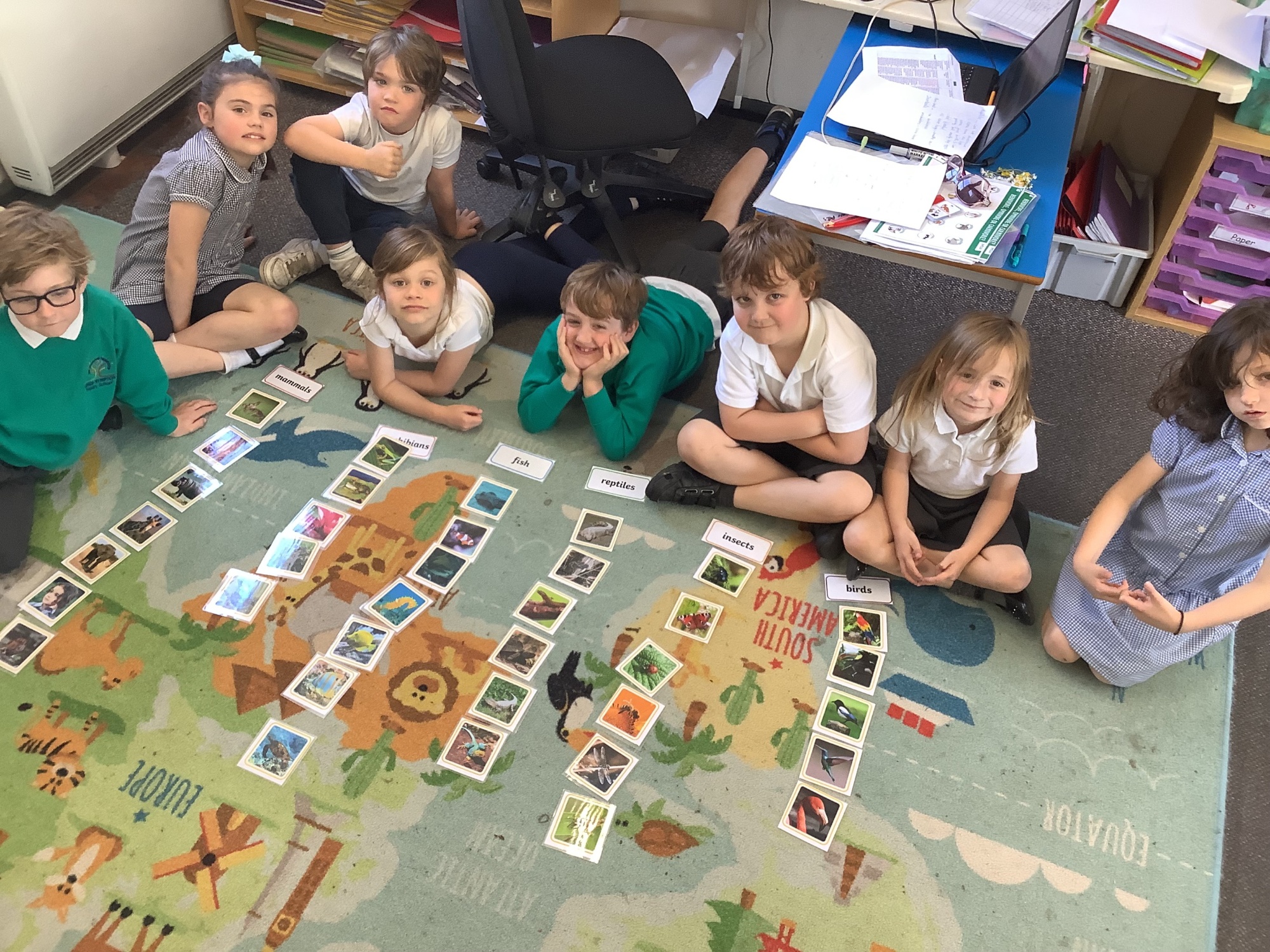 A picture of four children cutting and sticking coloured shapes onto paper