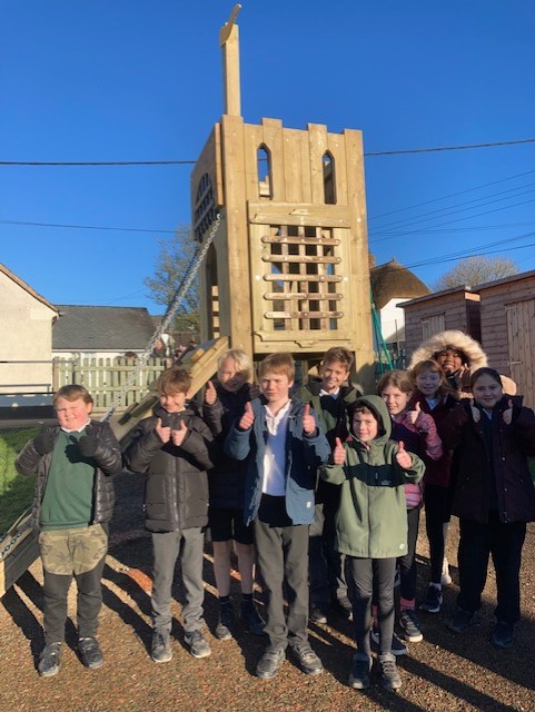 A group of children giving the thumbs up in front of a climbing tower in the playground