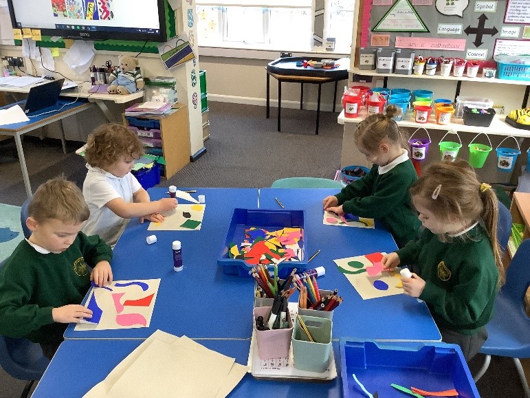 A picture of four children cutting and sticking coloured shapes onto paper
